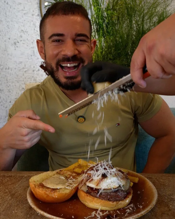 Pablo, de Cenando con Pablo, mientras le rallan queso sobre su hamburguesa en Hatillo